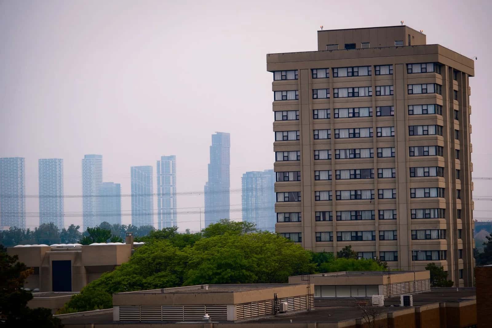 Modern high-rise towers on the horizon beyond a low apartment building and trees - ADU builders serving Vaughan, Ontario, Canada