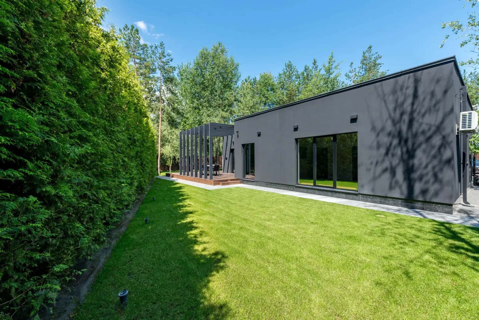 Modern black-clad detached garden suite with full-height glazing beside a hedged lawn, Ontario, Canada