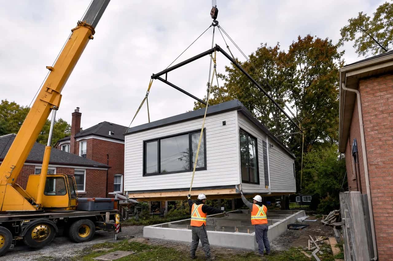 Crew in hi-vis vests guiding a modular dwelling unit as a crane sets it on a backyard foundation - modular ADU builders, Ontario, Canada