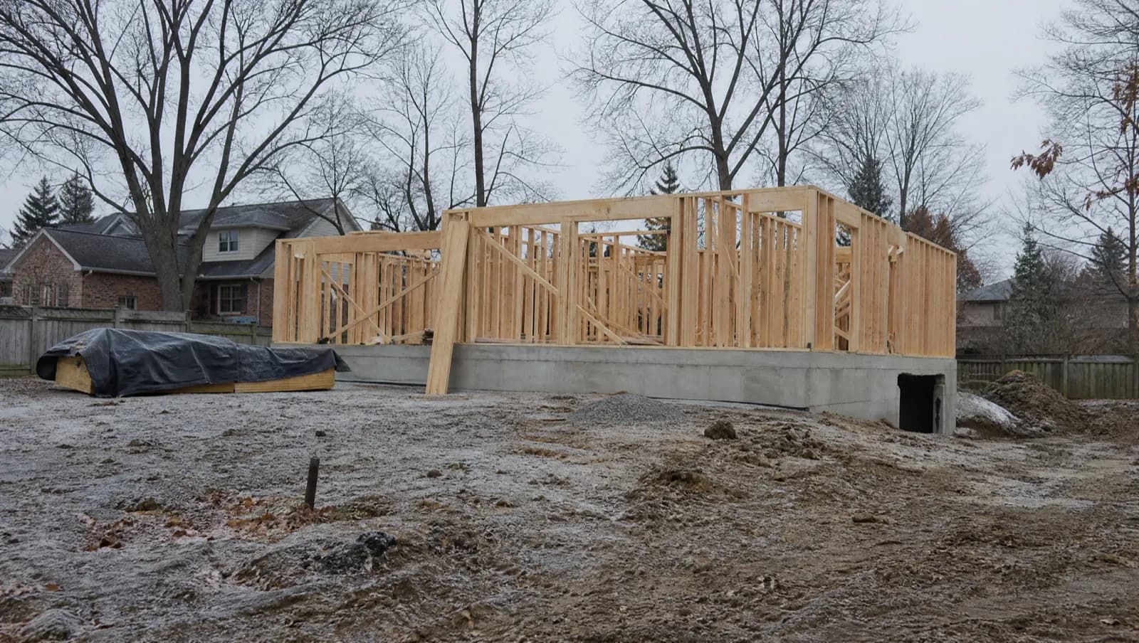Timber-framed backyard dwelling on a fresh foundation among bare trees in early spring - GTA ADU building season, Ontario, Canada