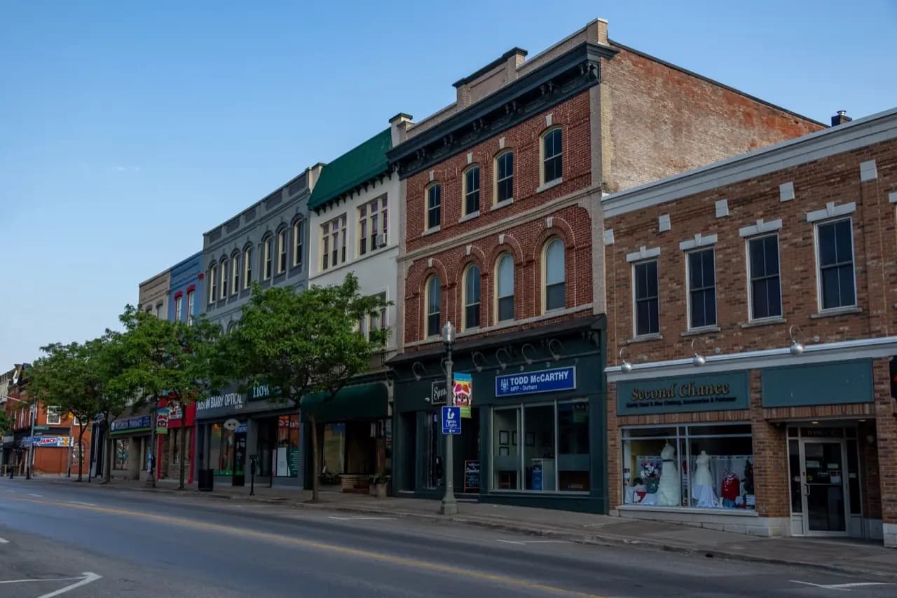 A wide downtown street of brick and stone buildings with cars at the curb - ADU builders serving Clarington, Ontario, Canada