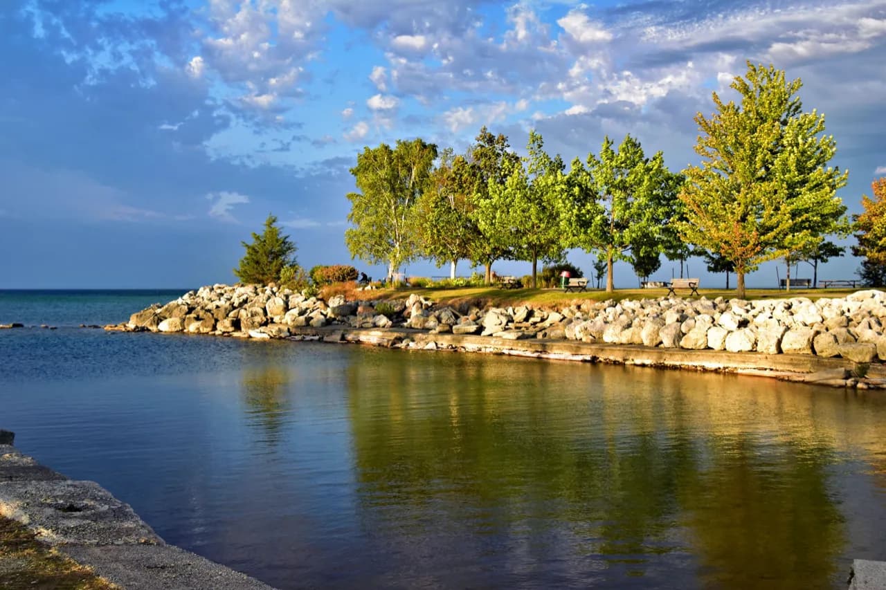 An armour-stone lakeshore park with maples turning colour above calm water - ADU builders serving Georgina, Ontario, Canada