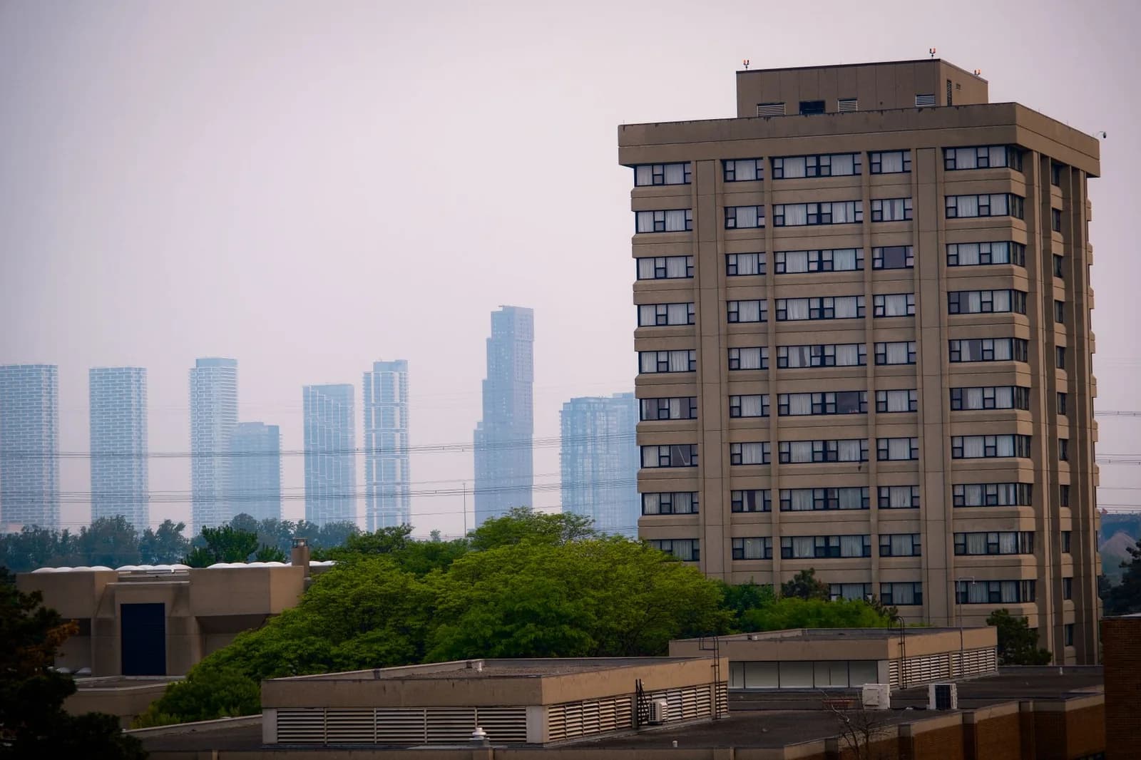 Modern high-rise towers on the horizon beyond a low apartment building and trees - ADU builders serving Vaughan, Ontario, Canada